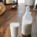 A glass bottle and a glass of milk on a wooden table.