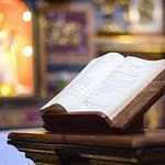 An open book on a wooden lectern with a blurred ornate background.