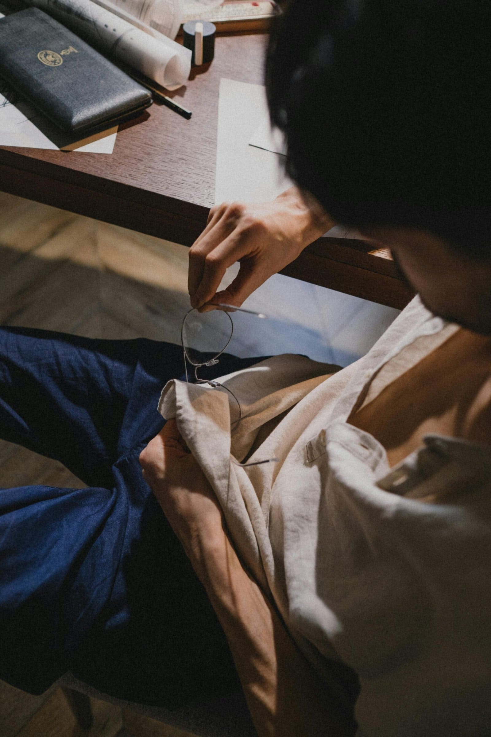 Person cleaning glasses with a cloth near a wooden desk with a notebook and other items.