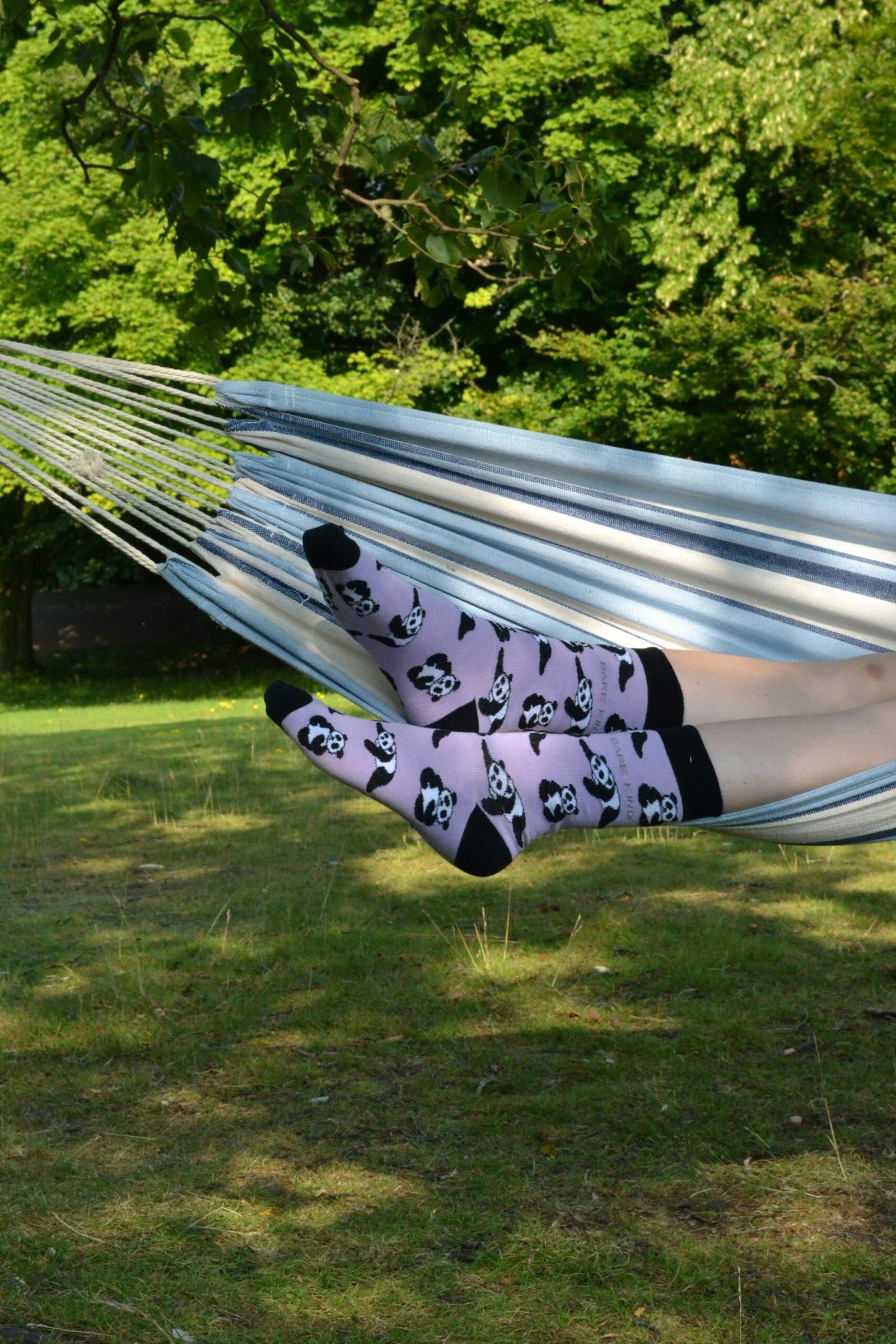 Legs wearing panda-patterned socks resting in a hammock outdoors in a lush garden.