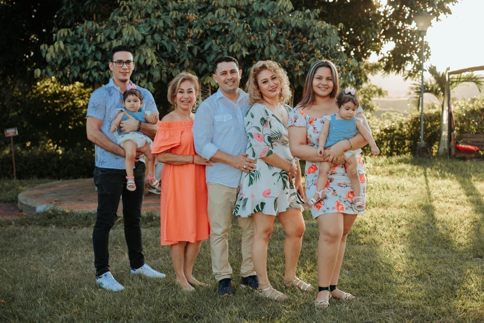 A group photo of six adults and two toddlers standing on grass with trees in the background.