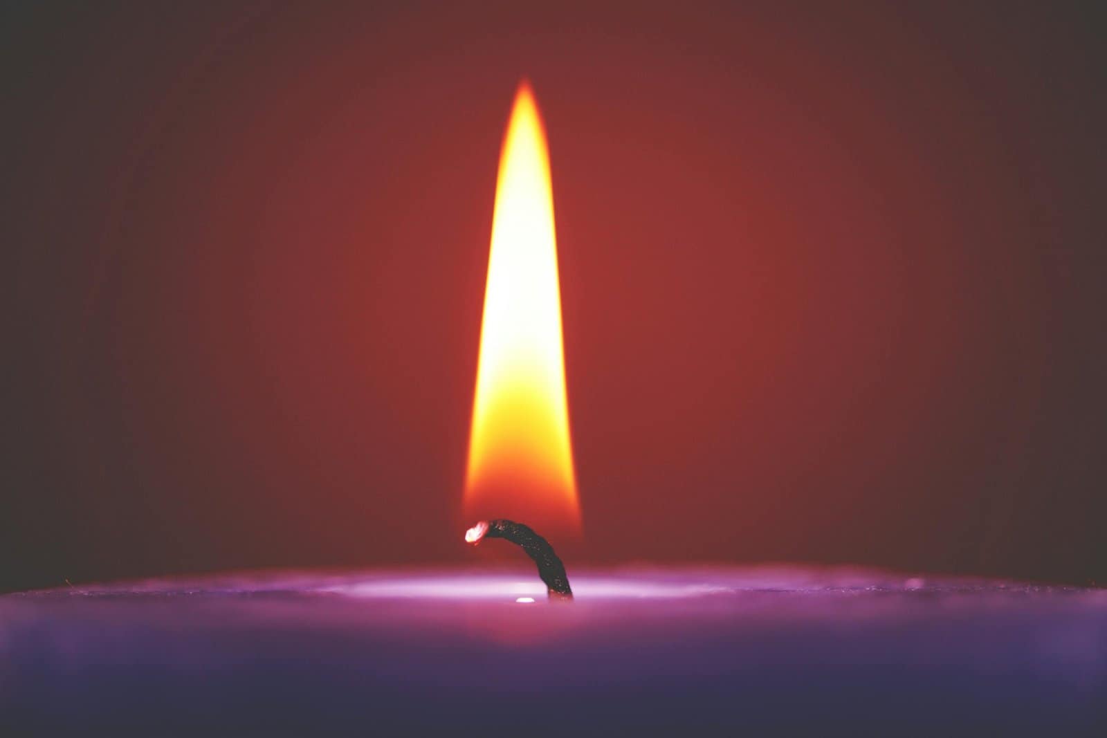 Close-up of a lit candle with a bright flame and a violet wax base.