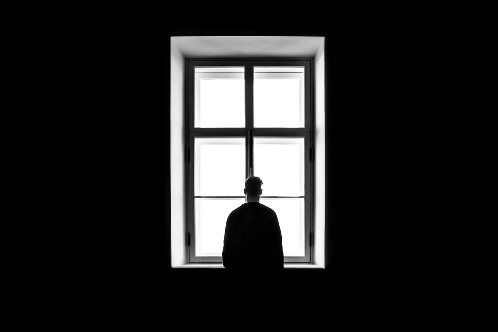 Silhouette of a person standing in front of a large, bright window with four panes.