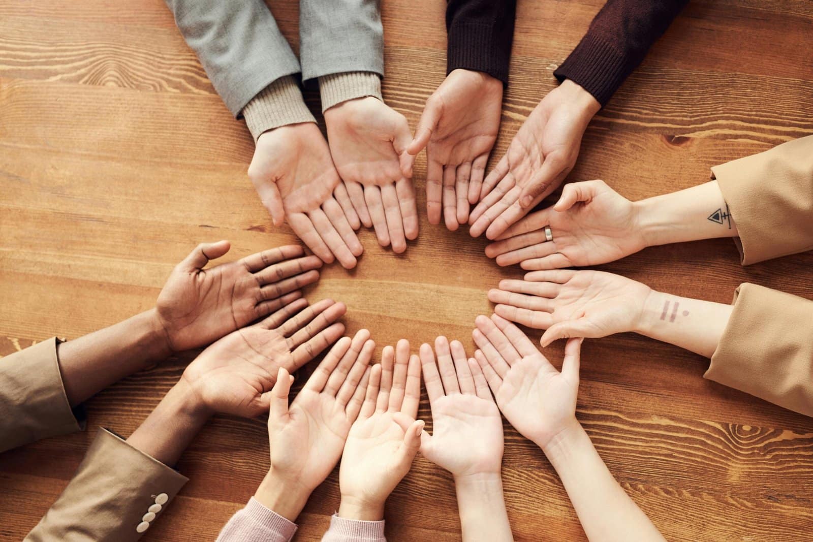 A circle of diverse hands with open palms on a wooden table.
