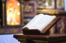 An open book on a wooden lectern with a blurred ornate background.