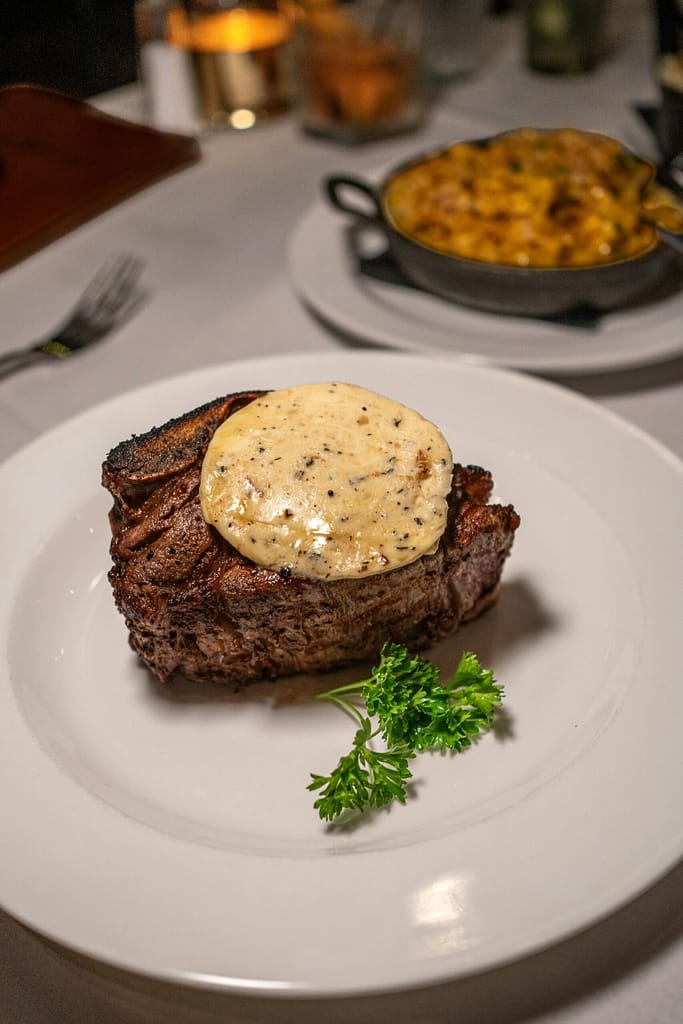 A juicy steak on a white plate, served with creamy macaroni and cheese on the side.